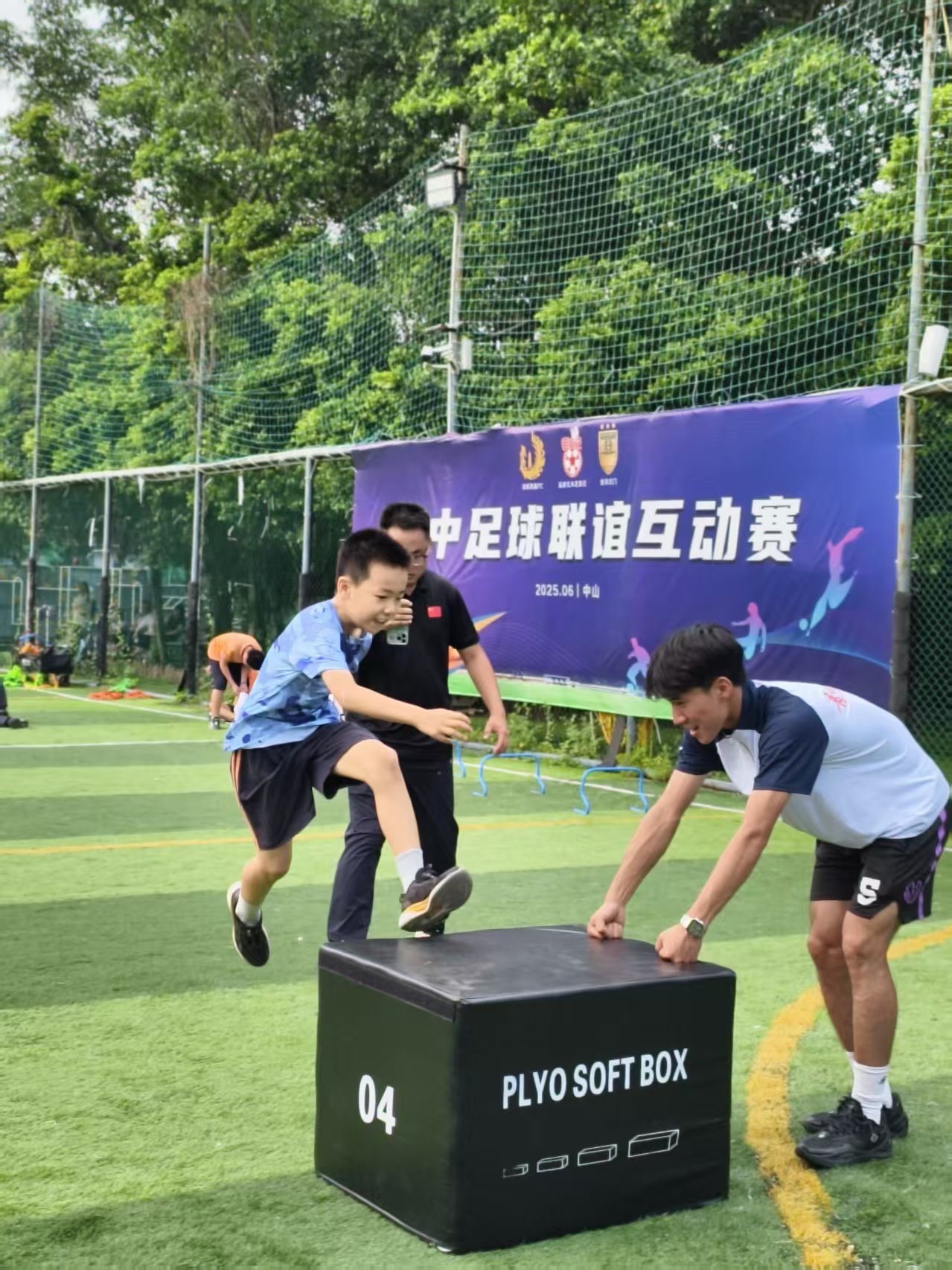 历史训练照片,一名参与者在黑色软箱前抬腿,旁边两名成人观察和协助